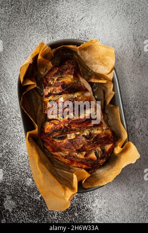 Pezzo di maiale cotto al forno con cipolla, aglio e timo su carta pergamena in un piatto ovale, vista dall'alto di un pezzo di carne cotto Foto Stock