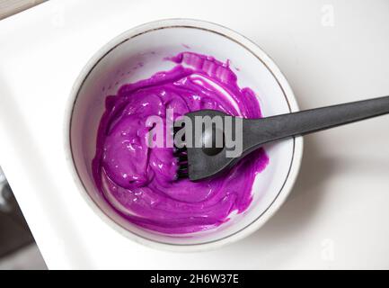 Ciotola in ceramica con tinture miste color pastello viola, dentro è spazzola dye, spazzola per colorare i capelli. Foto Stock