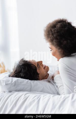 coppia interrazziale positiva sorridendo mentre si guarda l'un l'altro in camera da letto Foto Stock