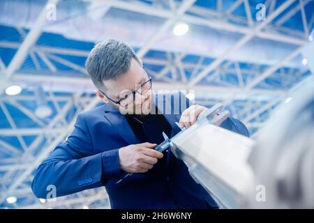 Concetto di controllo qualità dei prodotti fabbricati. Il tecnico controlla le dimensioni con calibro a corsoio al dettaglio della finitura dopo la lavorazione dei metalli sulla macchina cnc t Foto Stock