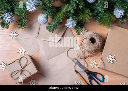 Concetto di Natale senza sprechi. Regali in scatole fatte a mano, carta riciclata, busta, spago, forbici, rami artificiali di abete rosso e fiocchi di neve di legno, a. Foto Stock