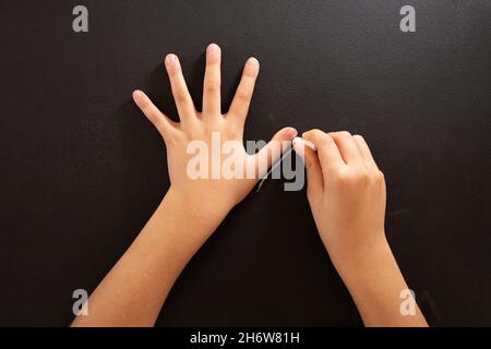 Un bambino traccia una mano con il gesso su una superficie nera, fai da te Halloween mestiere, tutorial passo 1 Foto Stock