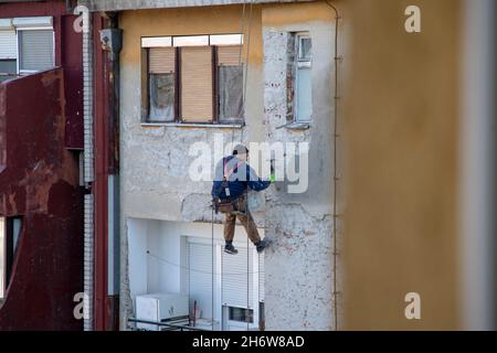 Belgrado, Serbia, 11 novembre 2021: Lavoratore appeso su corde di arrampicata rimuovendo un intonaco intemperie Foto Stock