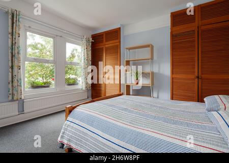 Cambridge, Inghilterra - Agosto 21 2019: Camera da letto in casa vittoriana britannica scarsamente arredata con armadi, letto e scaffalatura Foto Stock