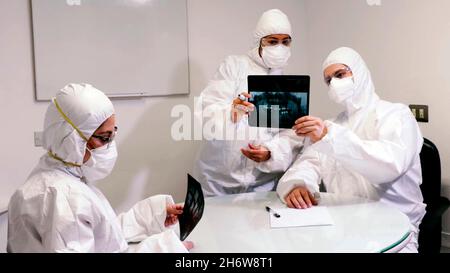 primo piano dei medici che osservano i raggi x in un ufficio con speciali tute antinquinamento Foto Stock