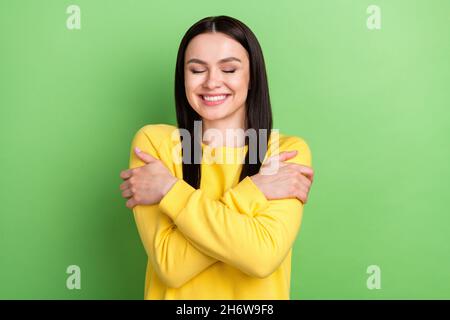 Ritratto di attraente sognante felice ragazza allegra abbracciarsi buon umore isolato su sfondo verde brillante Foto Stock