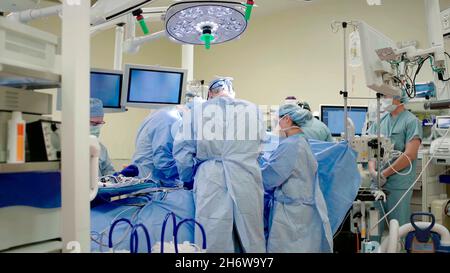 primo piano di medici, chirurghi, infermieri che operano su un paziente in una sala operatoria con monitor accanto a loro e studenti di medicina che osservano. Foto Stock