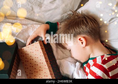 Ragazzo che dorme su biancheria da letto bianca con regali di natale Foto Stock