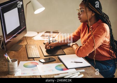 Freelance femminile che lavora su un nuovo design alla sua scrivania. Giovane designer grafico che si concentra su un tablet digitale con penna stilo. Creatività giovane WO Foto Stock
