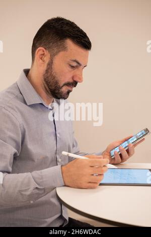 Giovane e attraente uomo d'affari che lavora con tablet e telefono cellulare. Foto Stock