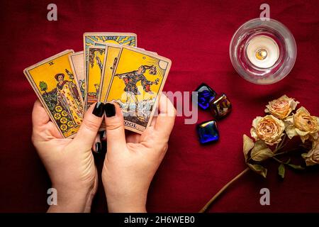 La mano del fortuneteller con manicure nero deposita le schede del tarot, il cristallo, la candela, le rose asciutte sul tablecloth rosso disposizione piatta in alto la vista della fortuna che dice, predire Foto Stock