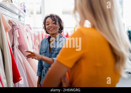 un felice assistente del negozio afroamericano che guarda il cliente offuscato in boutique Foto Stock