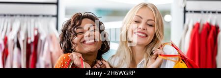 allegre donne interrazziali in possesso di borse shopping con acquisti in boutique di abbigliamento, banner Foto Stock