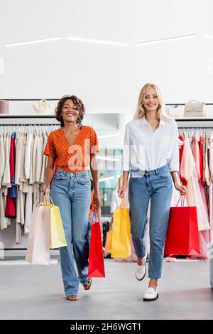 allegre donne interrazziali in possesso di borse shopping con acquisti in boutique di abbigliamento Foto Stock