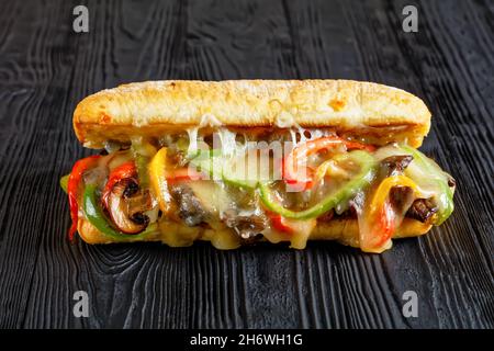 Sandwich con bistecca di formaggio Philly con manzo arrosto, pepe, cipolla caramellata, funghi e formaggio fuso su un tavolo di legno nero Foto Stock