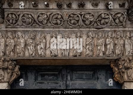 Santa Maria, affiancata da angeli e apostoli scolpiti, prega sull'architrave del portale centrale romanico del 1187 d.C. dell'ex Chiesa dei Santi Giovanni e Reparata in Piazza San Giovanni a Lucca, Toscana, Italia. La porta riccamente intagliata sopravvisse alla ricostruzione della facciata nel 1589. Foto Stock