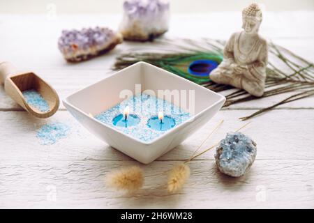 Cristalli di cera granulata blu e bianca per creare candele versando in ciotola e inserendo stoppino. Candela di sabbia fatta a mano in ciotola di ceramica bianca su bianco. Foto Stock