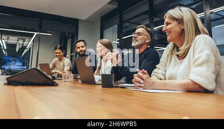 I professionisti allegri di affari ridono durante un briefing. Gruppo di uomini d'affari felici che si divertono a lavorare insieme in un ambiente di lavoro moderno. Squadra di div Foto Stock