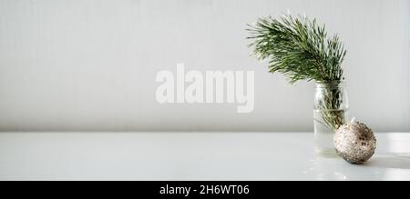 Zero rifiuti Natale banner web minimo con ramo di pino in vaso di vetro e ornamento palla di Natale su sfondo chiaro. Pino e scintille Foto Stock