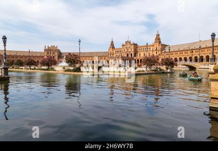 Siviglia, Andalusia, Spagna - 12 agosto 2021: Edificio rinascimentale centrale in piazza Plaza de Espana, vista sul fiume Guadalquivir con barche e gente Foto Stock