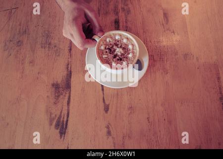 Vista dall'alto di una mano che tiene una tazza di cappuccino frumoso appena fatto in un bar Foto Stock