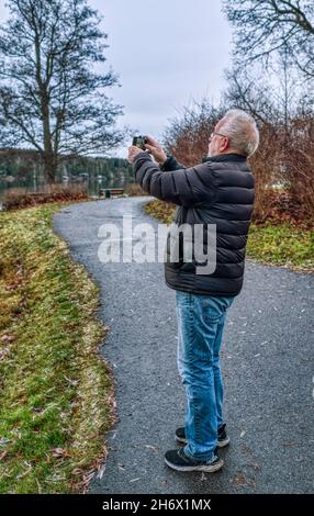 Uomo anziano scattando foto con il suo cellulare di paesaggio autunnale Foto Stock