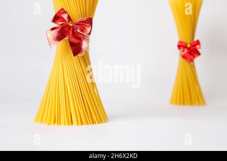 Un mazzo verticale, un mazzo di spaghetti crudi legati con una corda con un arco rosso. Fascio su sfondo bianco. Il concetto di cucina italiana per le vacanze. Foto Stock