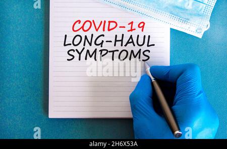 COVID-19 simbolo dei sintomi del codice a lunga distanza. Carta bianca con parole Covid-19 sintomi a lunga distanza. Mano del medico, penna, sfondo blu, spazio di copia. Medico, C. Foto Stock