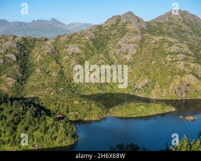 Cabina rossa solitaria al lago vicino mt. Sukkkertoppen, la montagna vicino a Hamn i Senja, Senaj isola, Norvegia Foto Stock