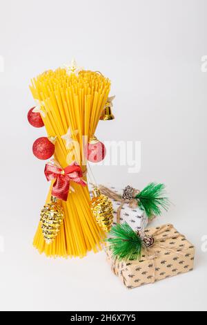 Un bouquet di spaghetti crudi a forma di albero di Natale con giocattoli, palline rosse e coni di pino. Albero di Natale fatto di cibo. Cucina italiana. Foto Stock