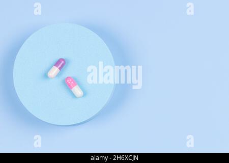 Podio a forma geometrica rotonda con capsule colorate di pillole medicinali su sfondo azzurro. Vista dall'alto, disposizione piatta, spazio di copia per il testo Foto Stock