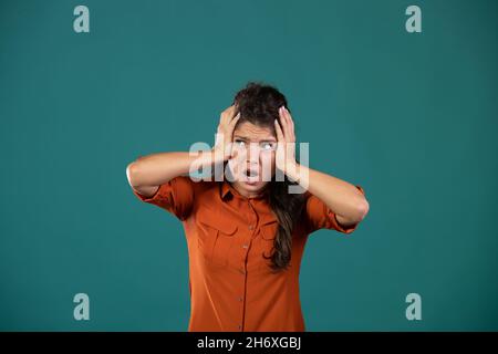 Giovane donna frustrato che tiene le mani sulla testa, concetto di follia, in studio su sfondo blu e guardando a lato Foto Stock