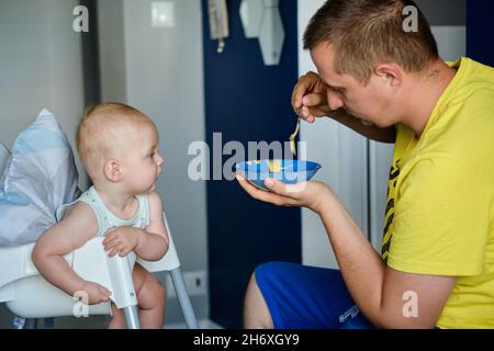 Un giovane padre nutre un bambino carino con cibo giallo per bambini Foto Stock