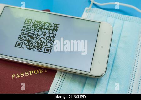 Uno smartphone con codice QR sulla vaccinazione del Covid-19 si trova sul passaporto e sulla maschera medica. Primo piano. Sfondo blu Foto Stock