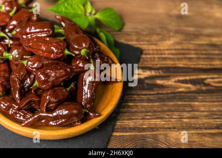 Peperoncino su sfondo di legno. Peperoncino extra caldo. Naga Bhut Jolokia Chocolate. Spezie esotiche. Ingredienti caldi per il cibo. Foto Stock