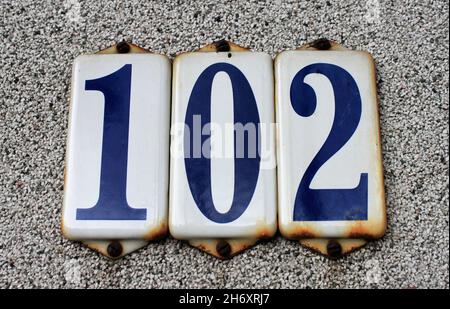 Il numero 102 in lettere blu sul cartello bianco smaltato sulla parete Foto Stock