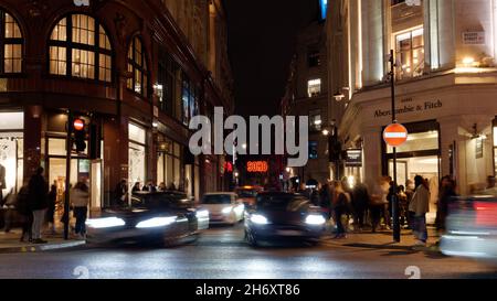 Auto che si allontanano da un bivio su Regent Street di notte offuscata da una lunga esposizione, con un cartello Soho. Londra Foto Stock