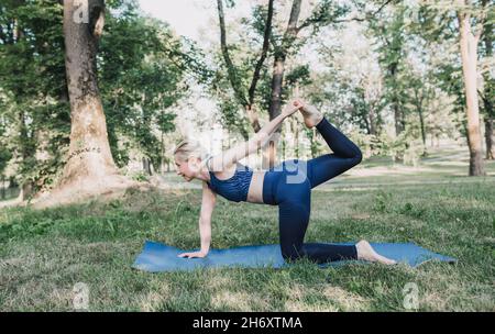 una giovane ragazza esegue complessi esercizi di yoga in un parco all'aperto. stile di vita sano Foto Stock