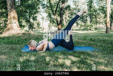 una giovane ragazza esegue complessi esercizi di yoga in un parco all'aperto. stile di vita sano Foto Stock