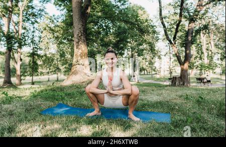 una giovane ragazza esegue complessi esercizi di yoga in un parco all'aperto. stile di vita sano Foto Stock