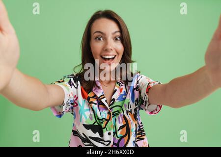 Giovane donna europea eccitata in camicia scattando foto selfie isolato su sfondo verde Foto Stock