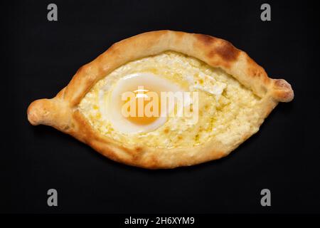 Il piatto nazionale georgiano è il khachapuri adjariano. Apri formaggio a forma di barca e torta di uova isolato su sfondo nero, vista dall'alto, primo piano Foto Stock