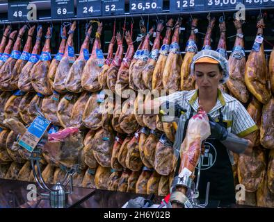 Donna che intagliano il prosciutto Iberico spagnolo con le gambe di prosciutto affumicato appese al supermercato, Andalusia, Spagna Foto Stock