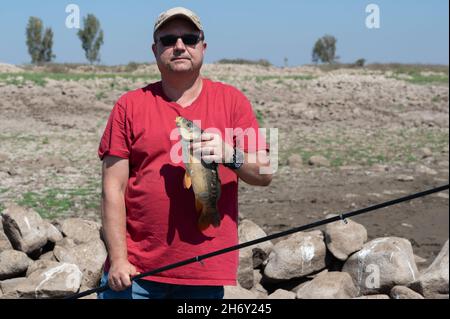 un pescatore felice ha preso un pesce su una canna da pesca e lo tiene in mano Foto Stock