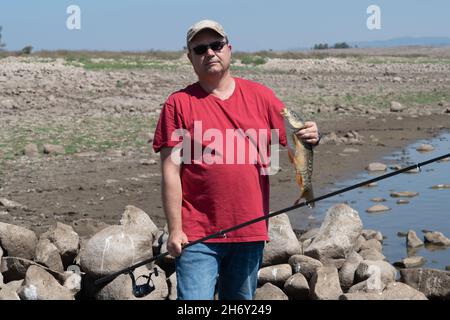 un pescatore felice ha preso un pesce su una canna da pesca e lo tiene in mano Foto Stock