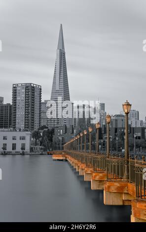 Il molo 7 di San Francisco è fiancheggiato da lampioni e da una ringhiera in metallo che conduce verso l'iconica Piramide Transamerica sullo sfondo. Foto Stock