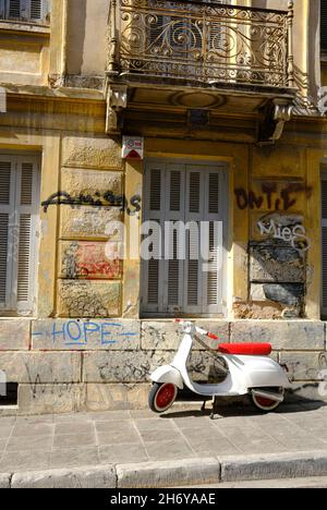 Uno scooter rosso e bianco parcheggiato di fronte ad un edificio con graffiti ad Atene, in Grecia Foto Stock