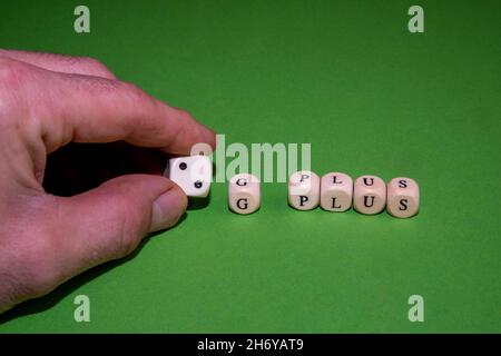 Concetto immagine 2G più controllo, uomo mano che tiene dadi e un cubo con la lettera G e la parola più, sfondo verde Foto Stock