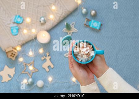 Mani femminili con una tazza blu di cacao con marshmallows Foto Stock