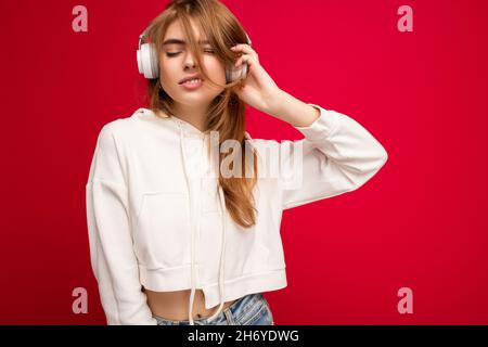 Foto di bella felice positivo fresco giovane bionda donna indossando felpa con cappuccio bianco isolato su sfondo colorato parete con spazio copia per il testo Foto Stock